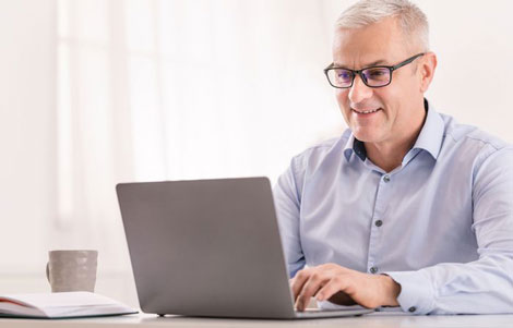 Older professional sitting at computer working with blue light glasses