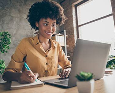 Woman using laptop smiling and writing with blue light contact lenses